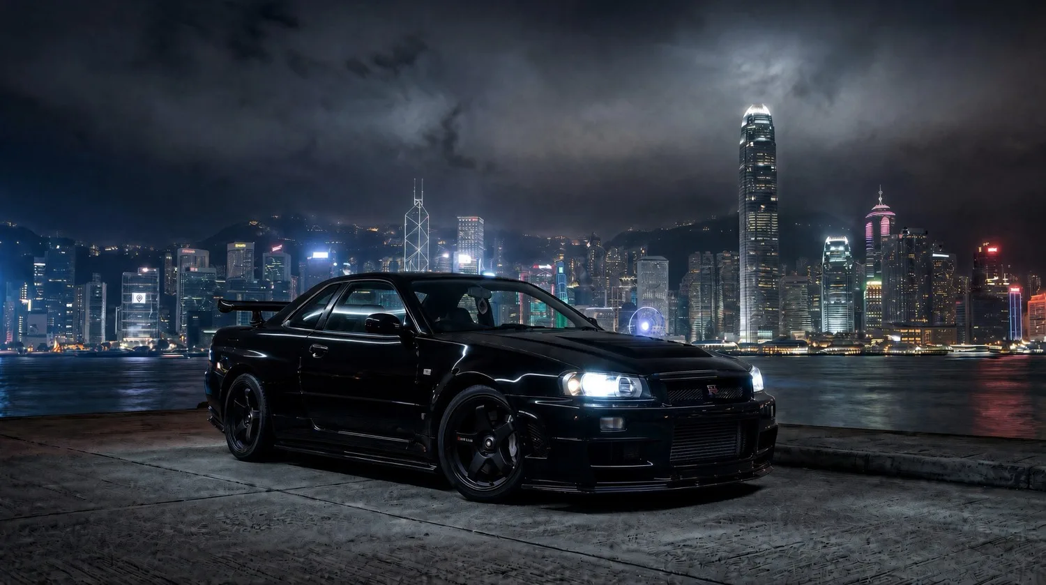 Our own black R34 Skyline GT-R project car at night in front of a city skyline.
