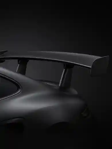 A carbon rear wing on a dark coupe in a studio.